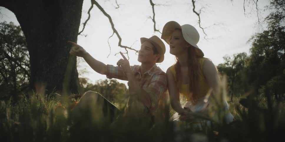 A man and woman sit and talk in a field under a tree