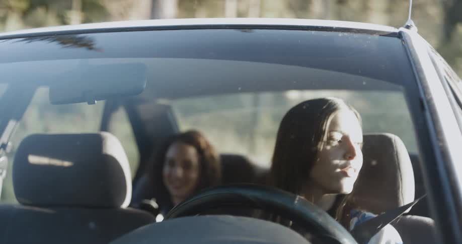 A woman with brown hair drives with another woman in the backseat