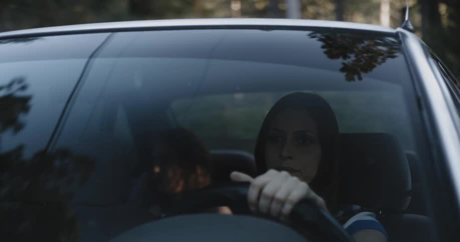 A woman drives a car with a passenger in the backseat