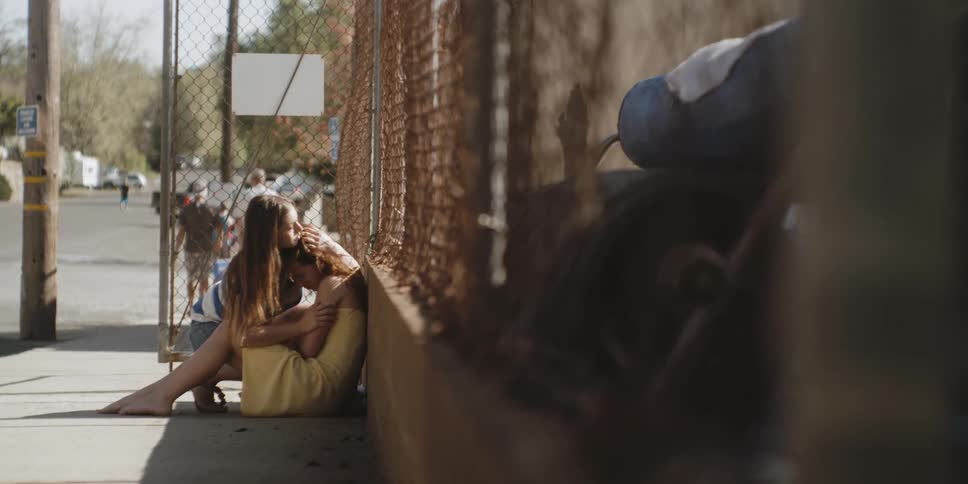 Two girls hug by a fence on a sunny day