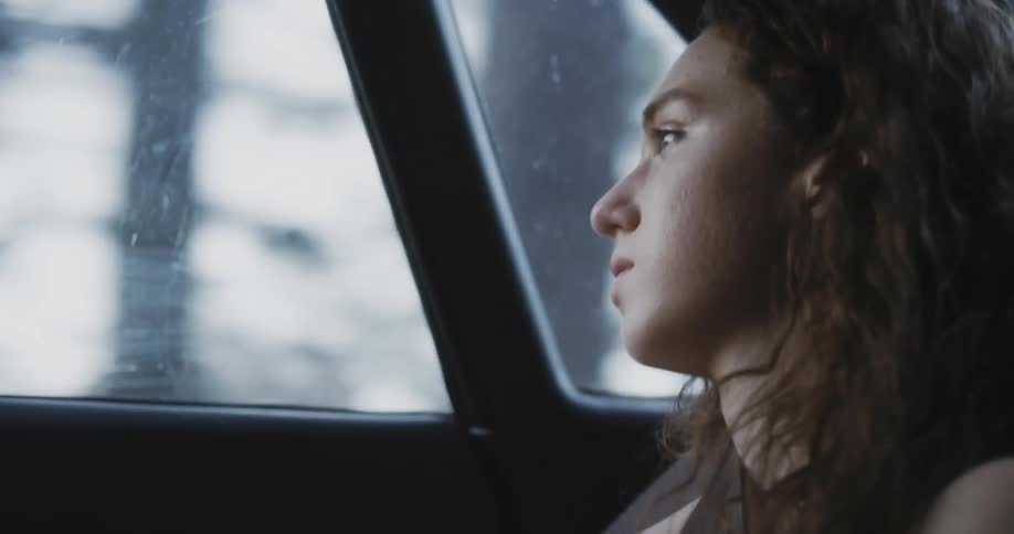 A woman rides in the back seat of a car and looks out the window