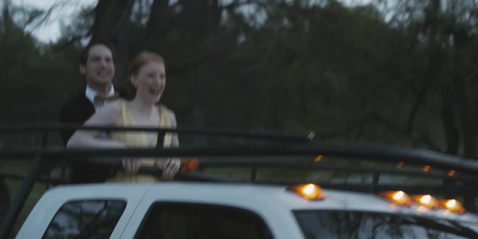A man and woman stand up on the back of a truck and laugh