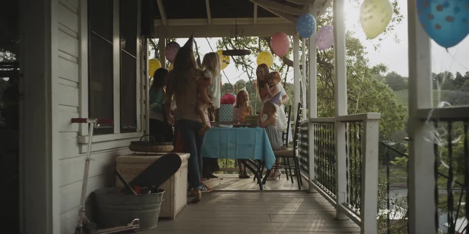 A woman carries a girl out to join the party on the porch
