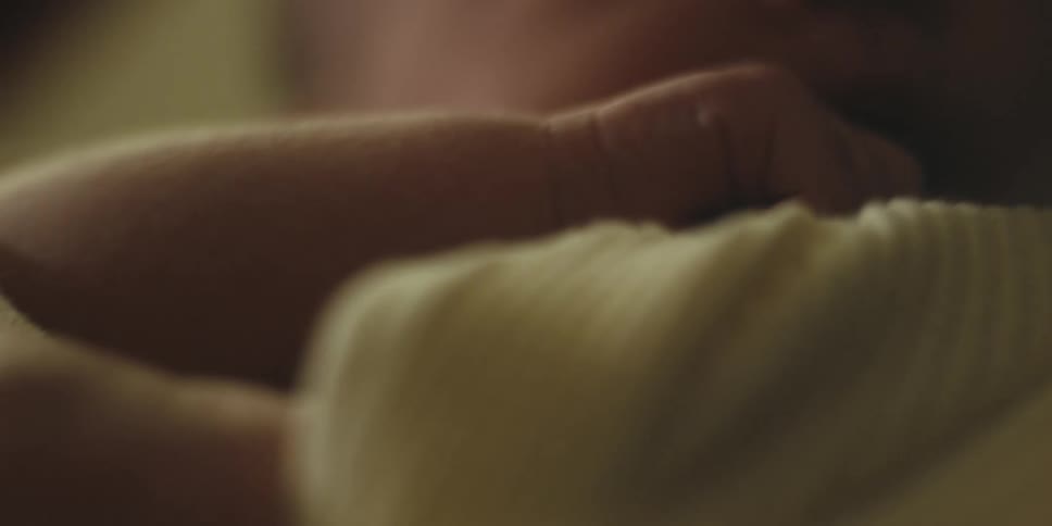 A baby puts its hand up to its mouth while being held