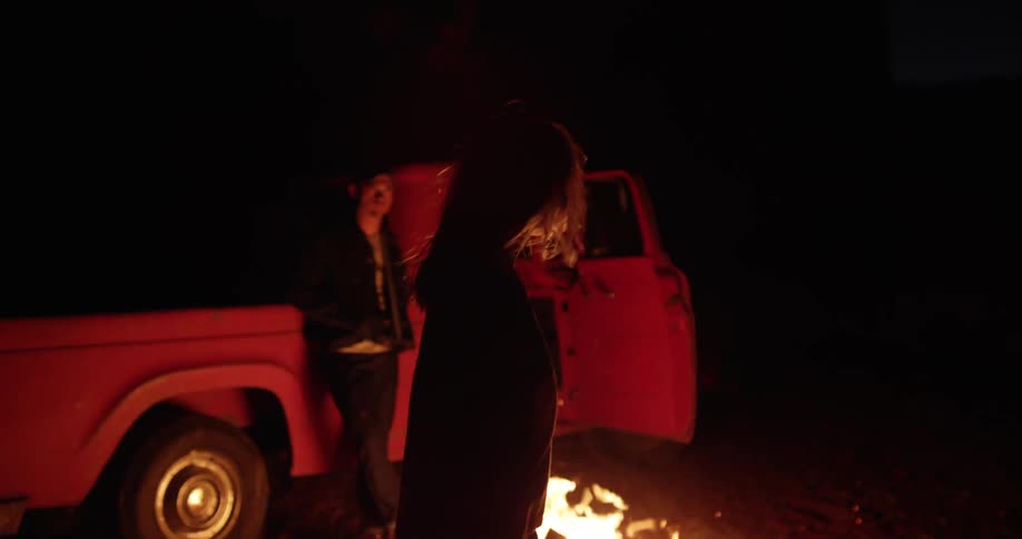 Man and woman standing near a fire at night