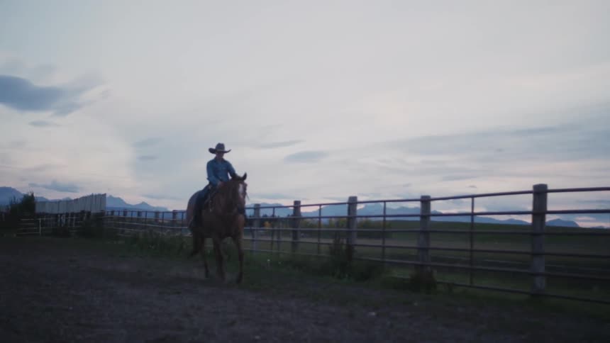 Young cowboy riding his horse as it trots alongside the fence