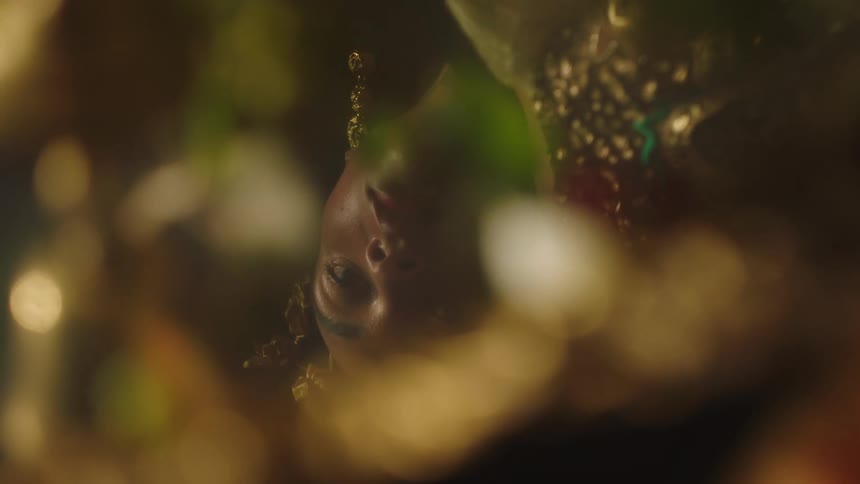 A woman wearing gold jewelry and headgear is reflected in a mirror