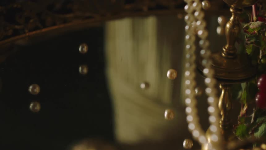 Pearls fall from a necklace onto the face of a mirror