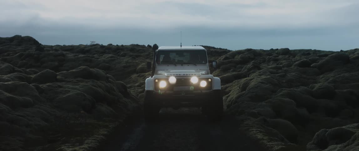 A vehicle parked on a dirt road through a rocky landscape on a cloudy day