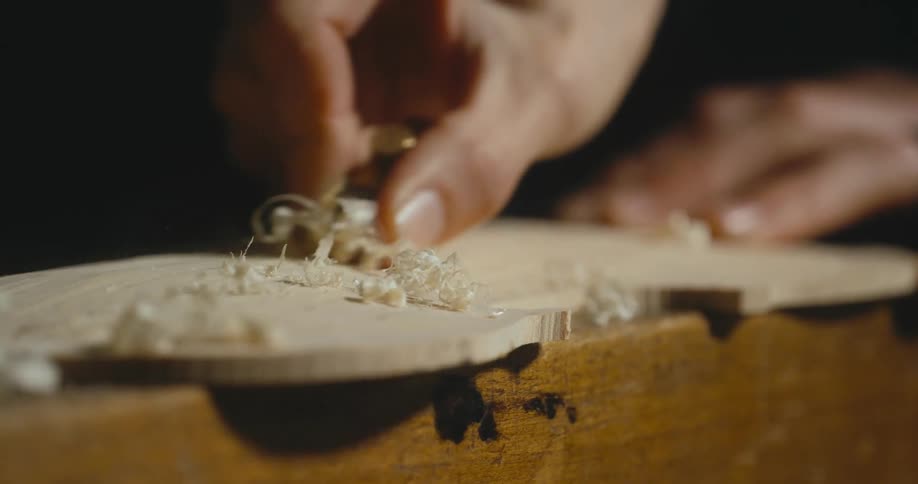 A man uses a small hand plane for woodworking causing curls of wood shavings