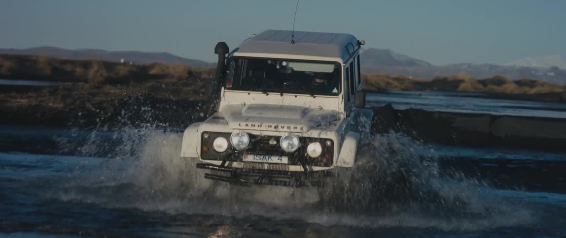 A car is driving off road through a small body of water
