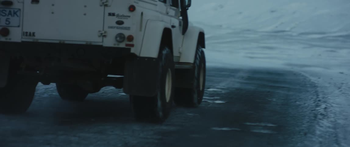 A land rover travels on an empty road through ice and snow covered landscape
