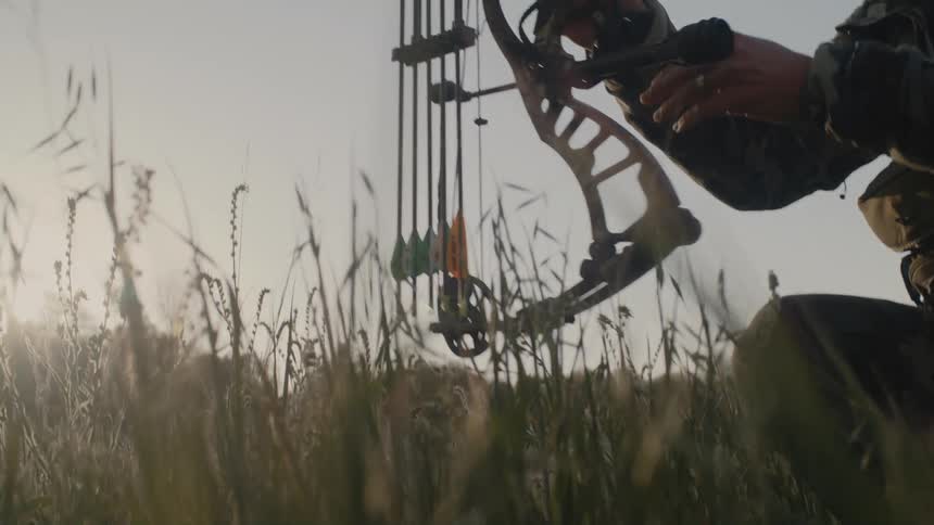 A person is in a rural area with a archery bow