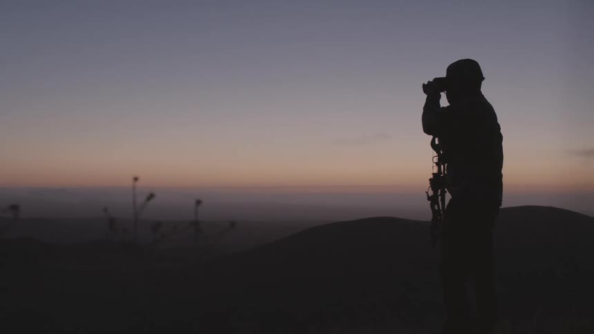 A man stands on the shore and looks out at the water through binoculars