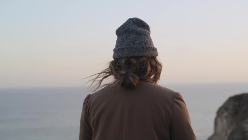 A woman is walking on the beach by the ocean at dusk