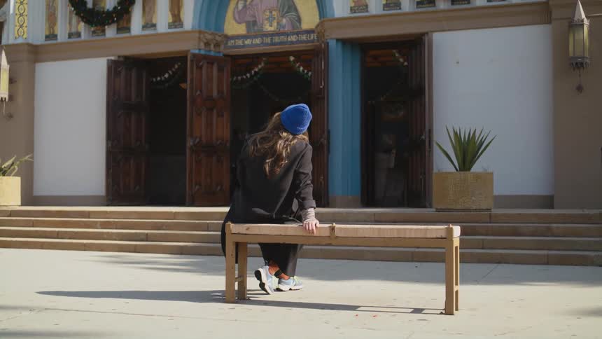 A woman is sitting on a bench outside of a store