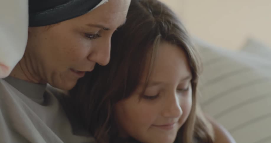 Mother with hair towel gray shirt reads book to daughter sitting on bed in bedroom