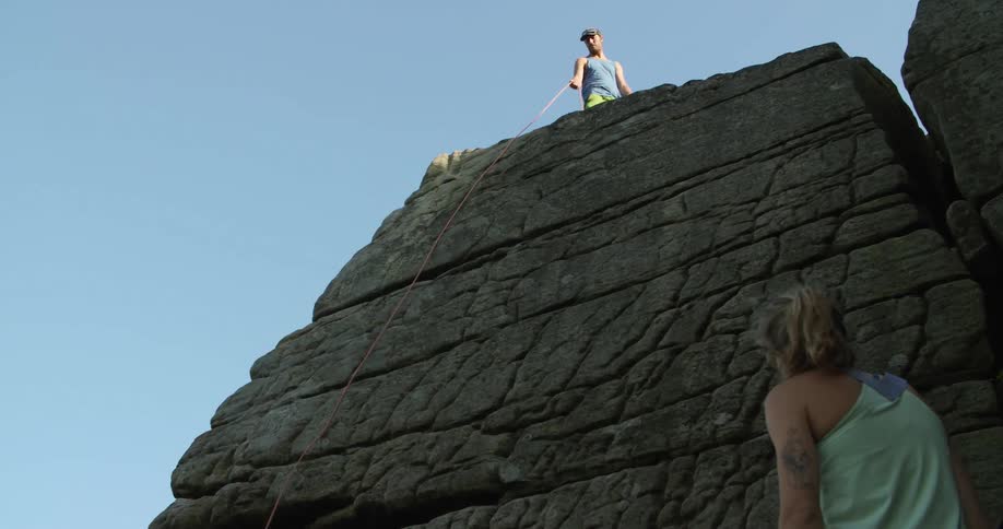 A male climber throwing a rope down to a female climber
