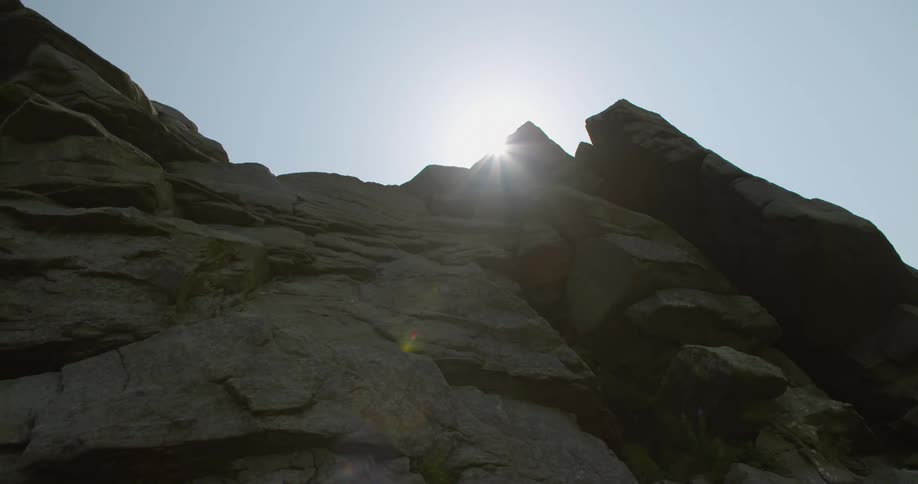 The sun shines and glares at the top of a sheer rock face