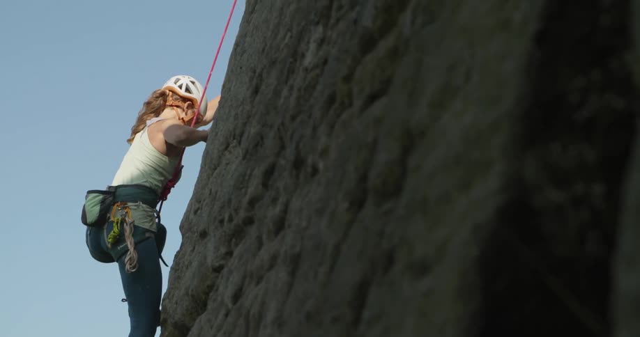 A female rock climber is climbing up the side of a mountain