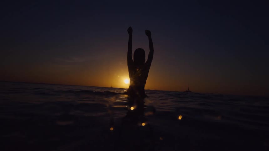 A woman holds her arms in the air while swimming in the ocean