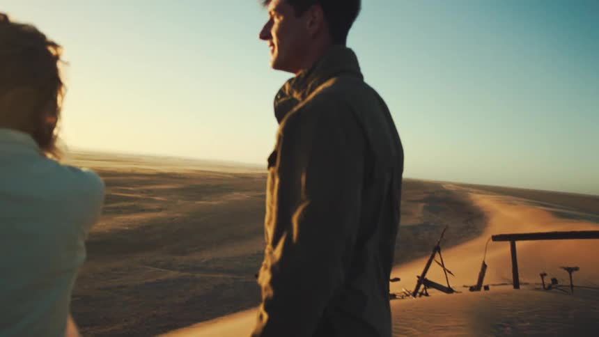 Man and woman look out over desert landscape at sunset