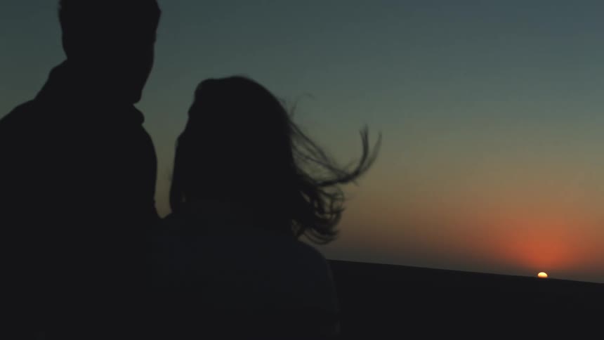 A couple watch a romantic sunset on windy evening