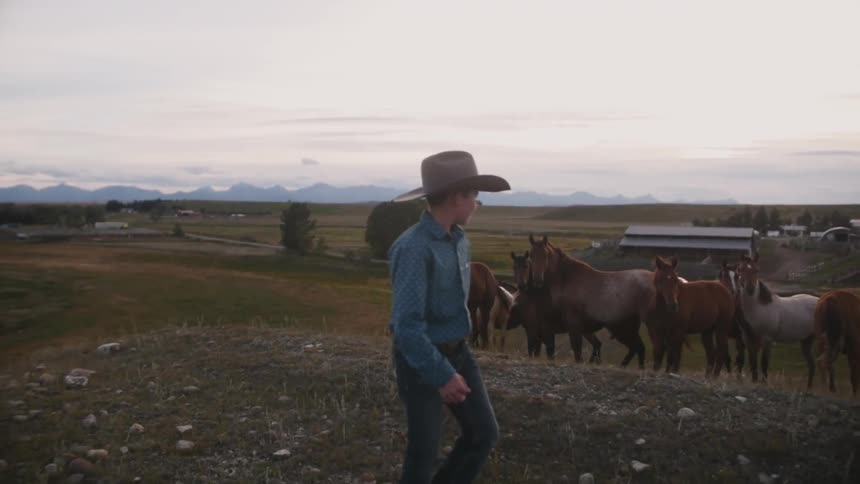 A boy is walking past some horses n a farm