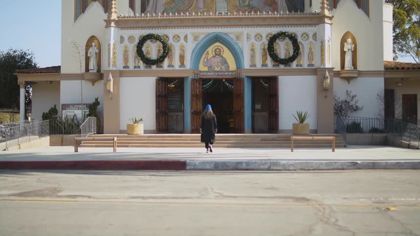 Woman wearing a hat and coat walks towards a church that has a mural of jesus above the entrance
