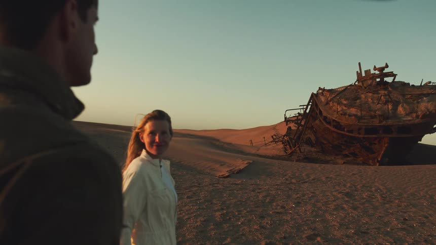 Man and woman share a moment as they explore a desert shipwreck