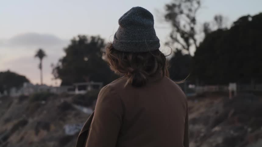 Woman with gray wooly hat brown hair and jacket looks at valley at dusk