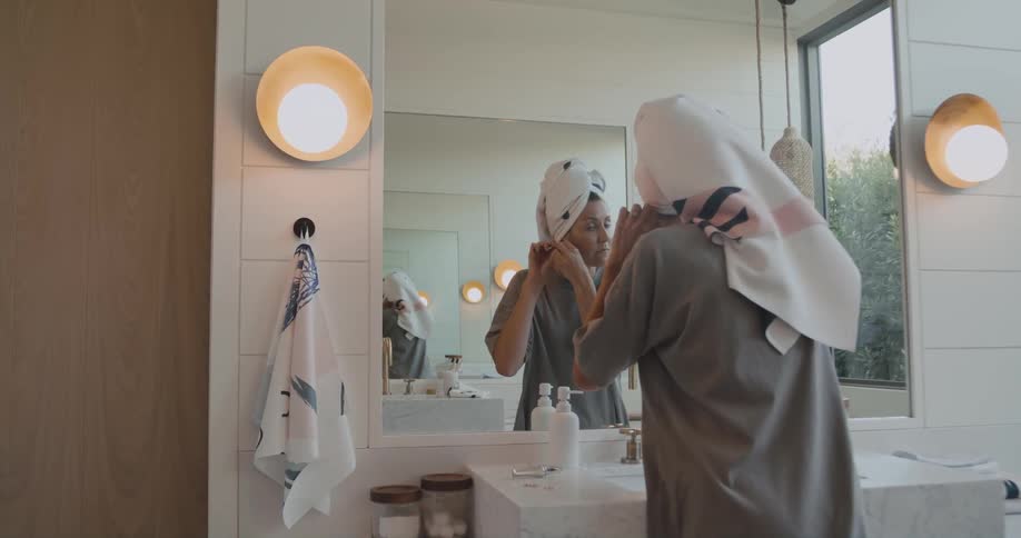 Woman stands in bathroom putting on earrings