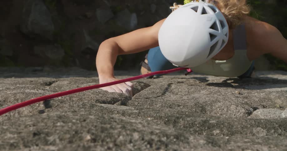 A woman looks for holds while climbing up the side of a mountain