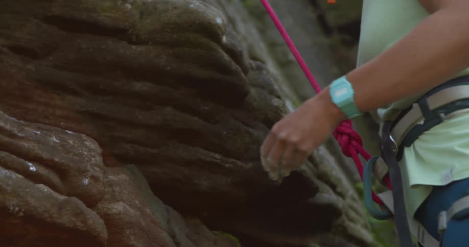 A climber dusts her hands with some chalk while looking up the rock face