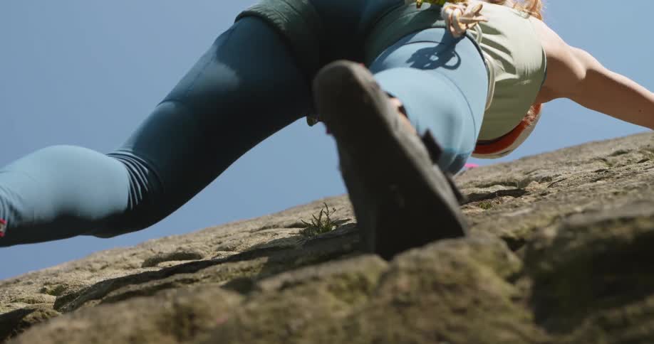 A woman rock climbing on a cliff looks down as she moves her foot