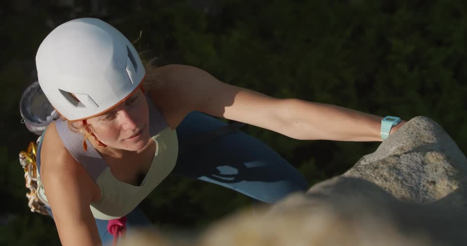 Female climber wearing safety equipment climbs a rock face in wilderness