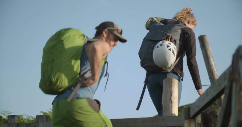 A man and woman out hiking climb over a fence
