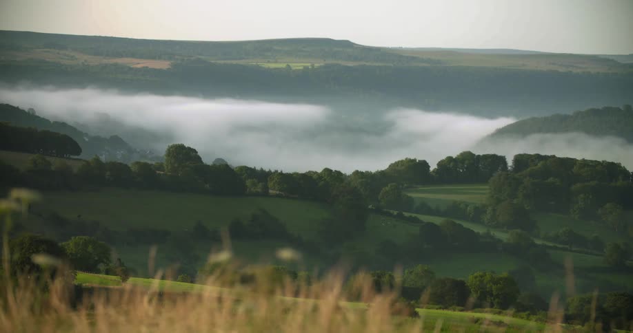 Aerial view of an open landscape with fog and hills is displayed