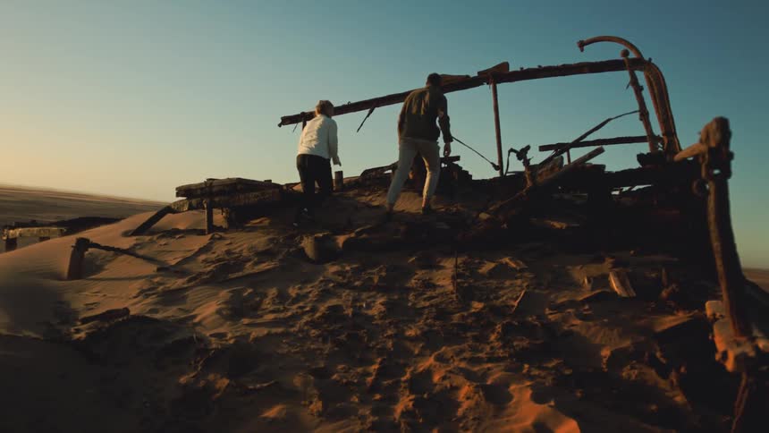 Man and woman explore shipwreck debris in windy desert