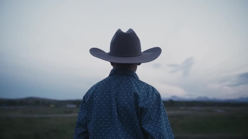 Young cowboy standing alone looking out at the horizon