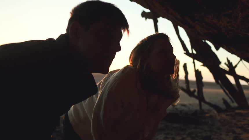 Man and woman explore desert shipwreck at sunset