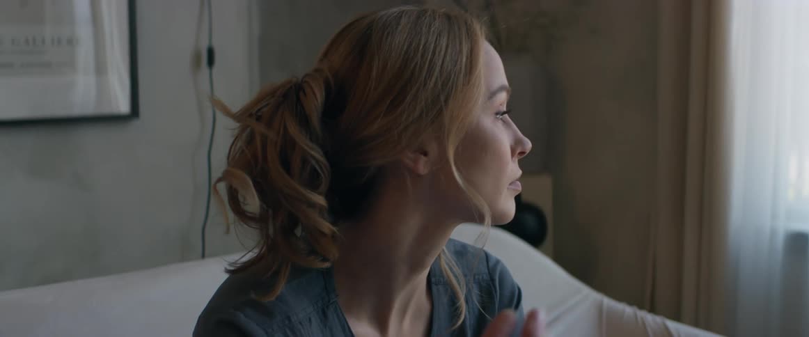 Woman sitting on couch wipes her eyes as she looks around and down