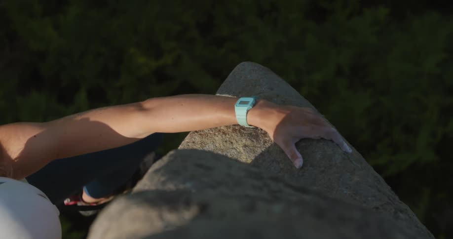 A woman wearing a white helmet grips the rocks on a cliff that she is climbing