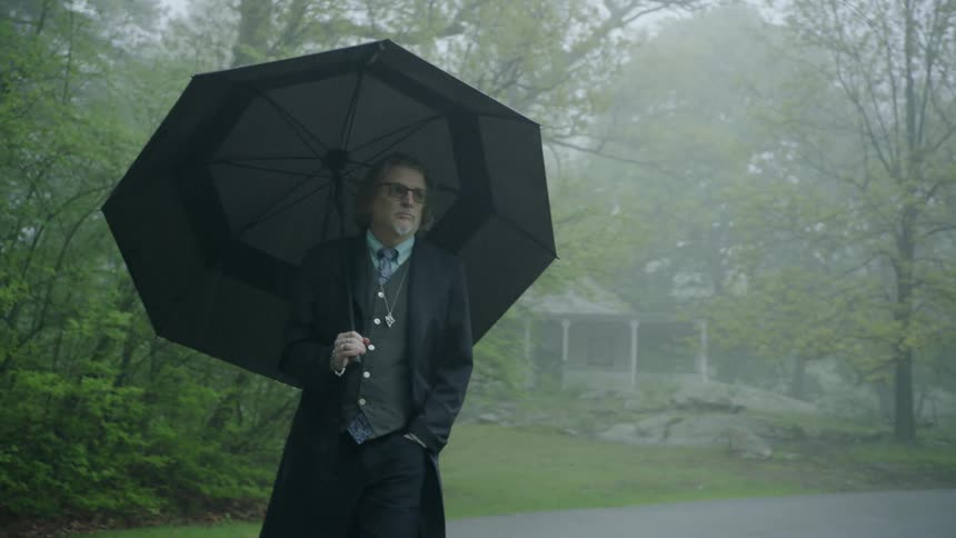 A man in a suit walks in the rain down a rural road