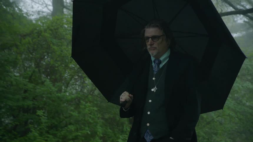 Man wearing glasses and carrying umbrella walks along foggy road in the rain