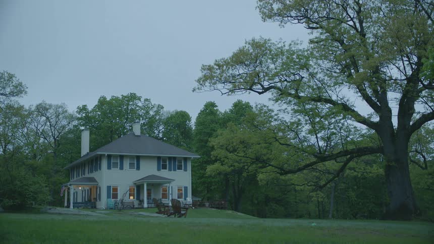A house with grass in the foreground with trees the sky and clouds in the background