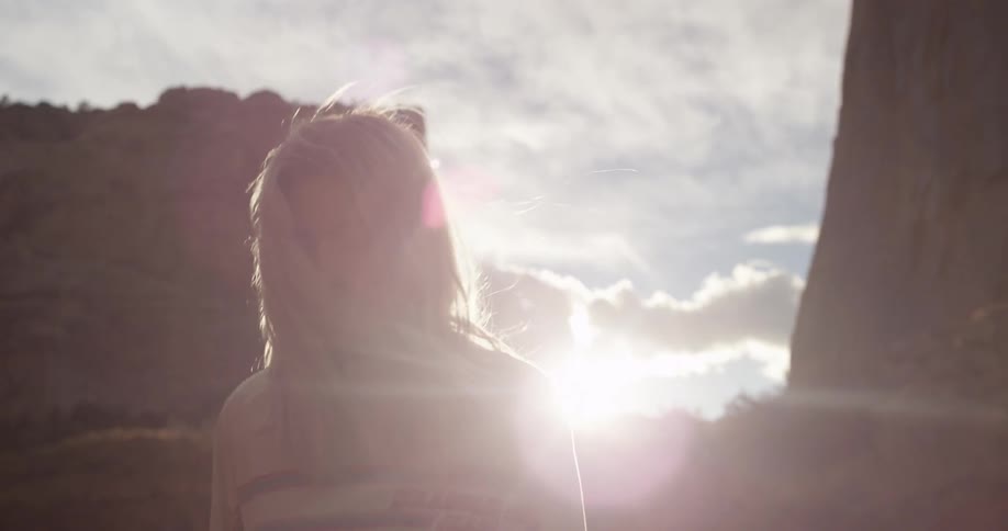Blonde woman walking away from two large rocks at sunset