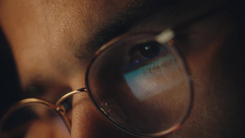 The monitor of a computer is reflected on the eyeglasses of a man as he scrolls up and down