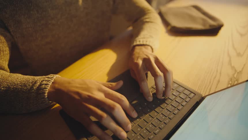 Man with a beard and wearing glasses sits at a desk and types on a laptop