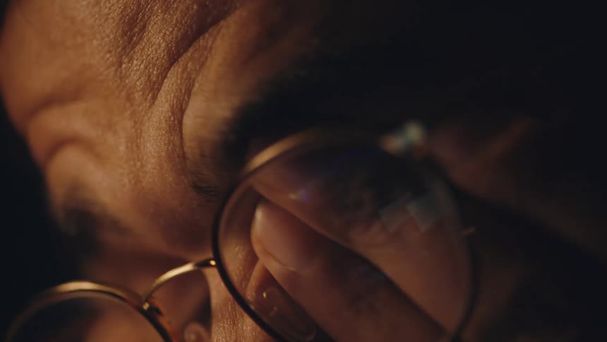 Close up of a man rubbing his eyes with his fingers under the glasses reflecting a computer screen